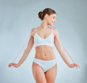 Woman in white activewear holding a measuring tape, smiling and looking confident.