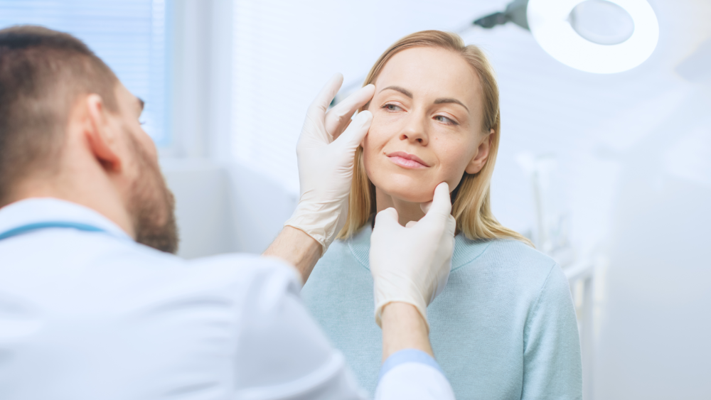 Doctor examining woman's face during a facelift consultation.