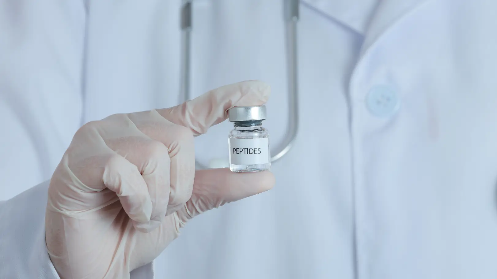Gloved hand holds a small vial labeled peptides in front of a healthcare professional wearing a white coat.