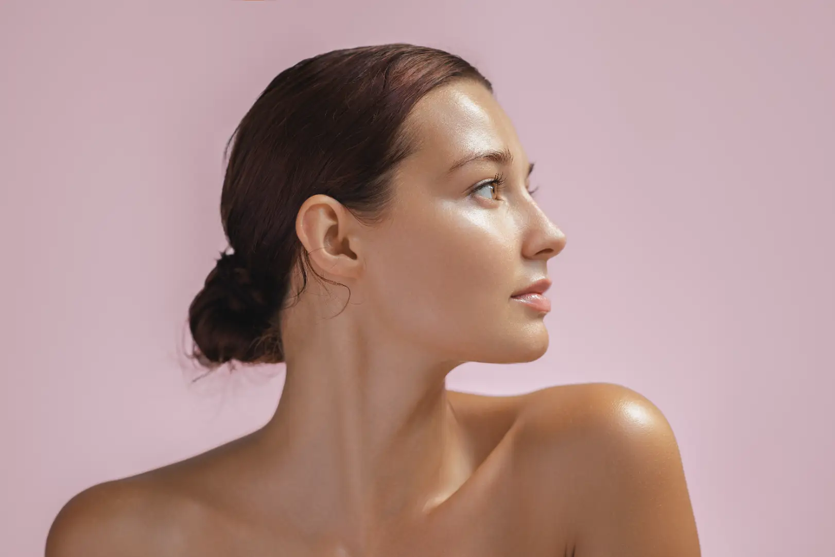 Side profile portrait of a woman with hair tied back against a light pink background.